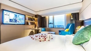 A hotel room with a large bed, a TV mounted on the wall, a city view through the window, and a small table with a chair. - Yinjiang PLUS Hotel (Hangzhou)