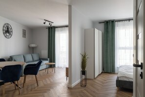 Ein moderner, gut beleuchteter Raum mit einer Couch, Sesseln, einem kleinen Tisch, einer Zimmerpflanze und einem Bett.