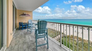 A balcony with a view of the beach, featuring a table and chairs, and a striped umbrella. - Majestic Beach Towers 2-404 (Panama City Beach)
