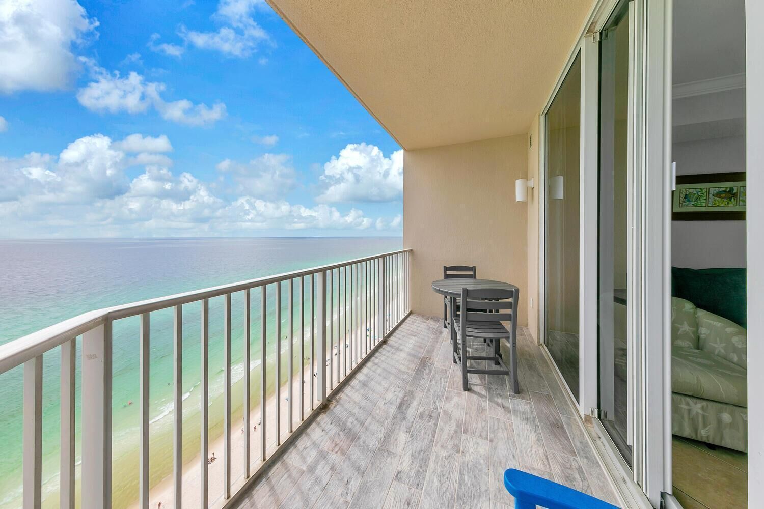 A balcony with a view of the ocean, a table with chairs, and a sliding glass door leading to a room with a green couch.