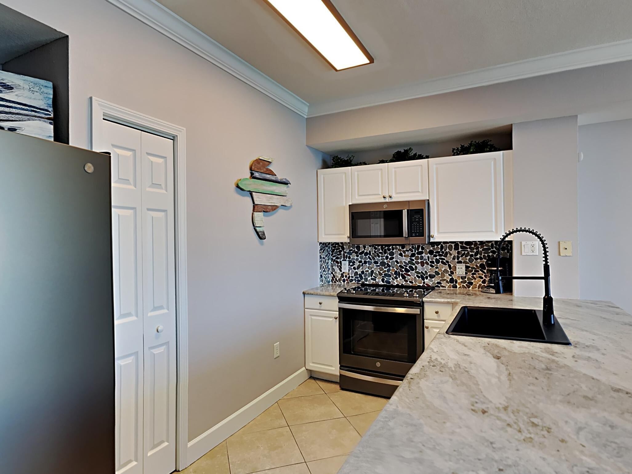 A kitchen with white cabinets, a microwave, an oven, and a marble countertop.