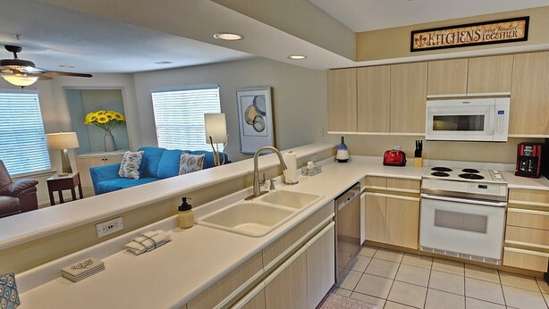 A modern kitchen with a built-in microwave, stove, and sink. There is a dining area with a blue sofa and a ceiling fan. - Fairways Paradise Walk-in Suite at the Fairways at Thousand Hills! Great Rates! (Branson)