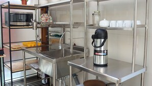 Een keuken met roestvrijstalen apparatuur, een spoelbak en planken met servies en een koffiezetapparaat.