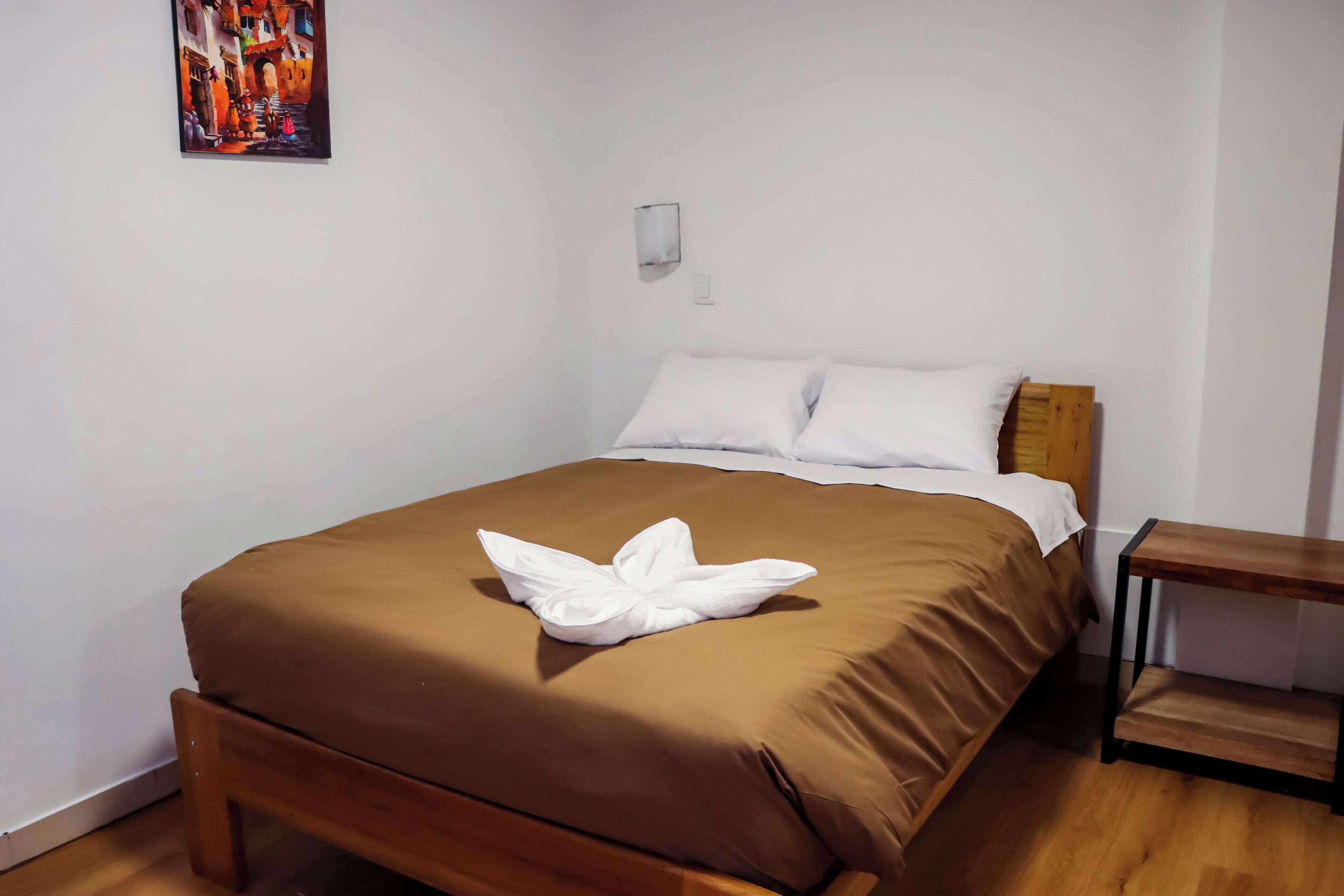 Un lit bien fait, recouvert d’une couverture marron, avec une serviette blanche pliée posée sur le dessus.