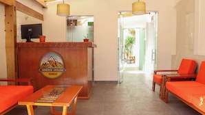 Een receptiegedeelte met een houten toonbank, twee oranje banken en een bord met de tekst 'Andes House Cusco'.