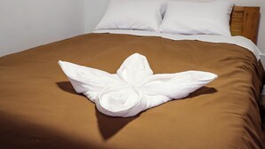 Een net opgemaakt bed met een bruine plaid en een handdoek gevouwen in de vorm van een bloem.