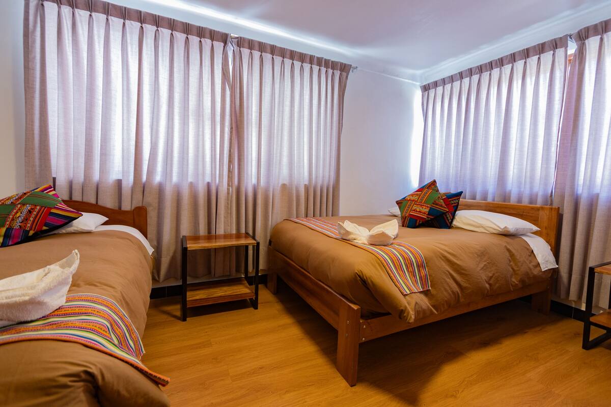Ein Hotelzimmer mit zwei Holzbett, jedes mit einem Holzgestell, einem kleinen Nachttisch und einer bunten, gestreiften Decke.