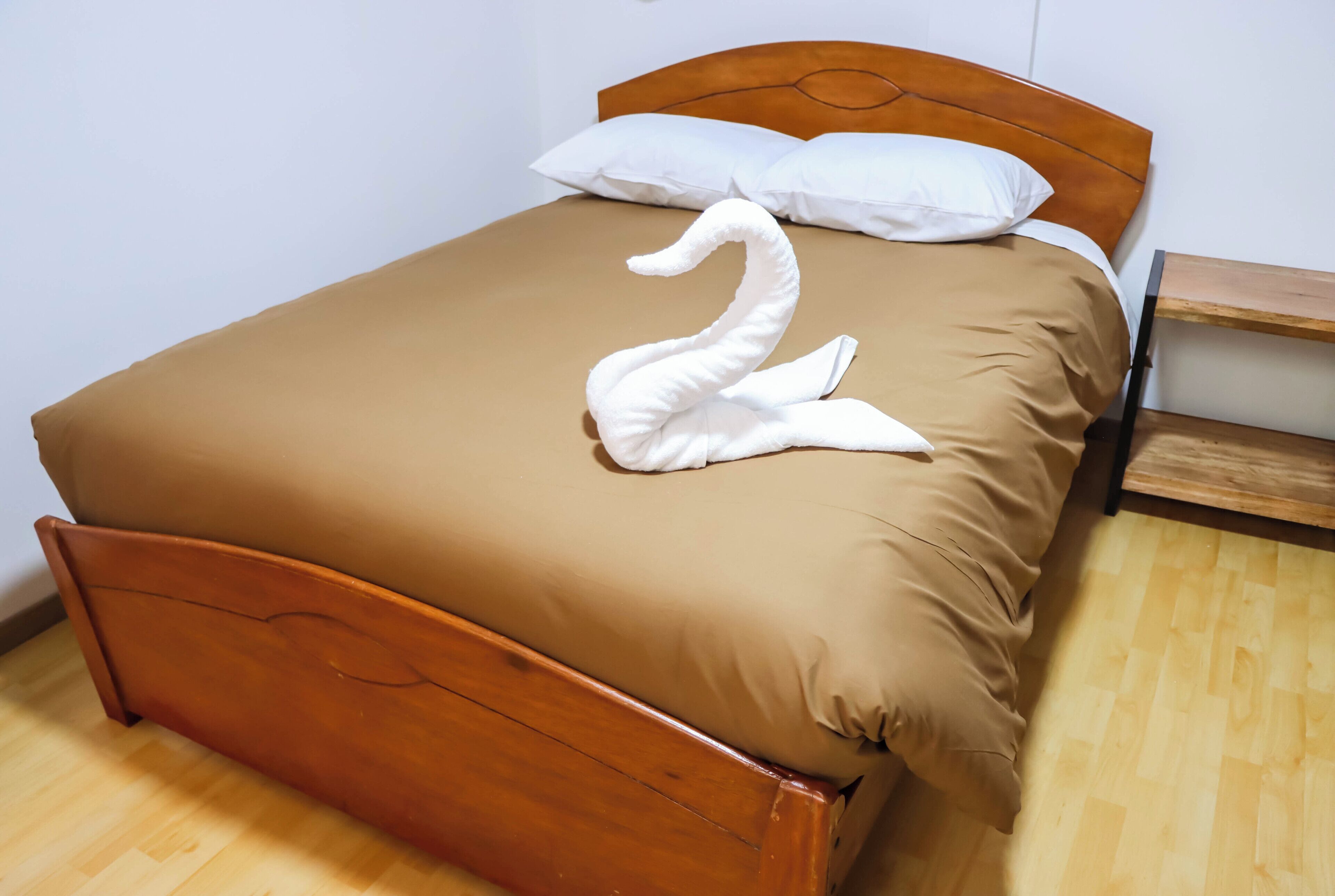 Una cama bien tendida con una colcha marrón y un almohadón con forma de cisne blanco.