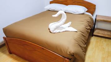 Una cama bien tendida con una colcha marrón y un almohadón con forma de cisne blanco.