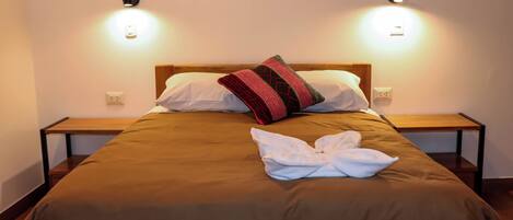 Una cama bien hecha con una colcha marrón, una almohada blanca y una almohada decorativa. Hay dos mesitas de noche con lámparas a cada lado de la cama.