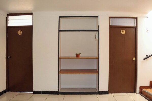 A hallway with three doors, each marked with a number. There is a shelf unit in the center with a small plant on the top shelf. - Andes House Cusco (Cusco)
