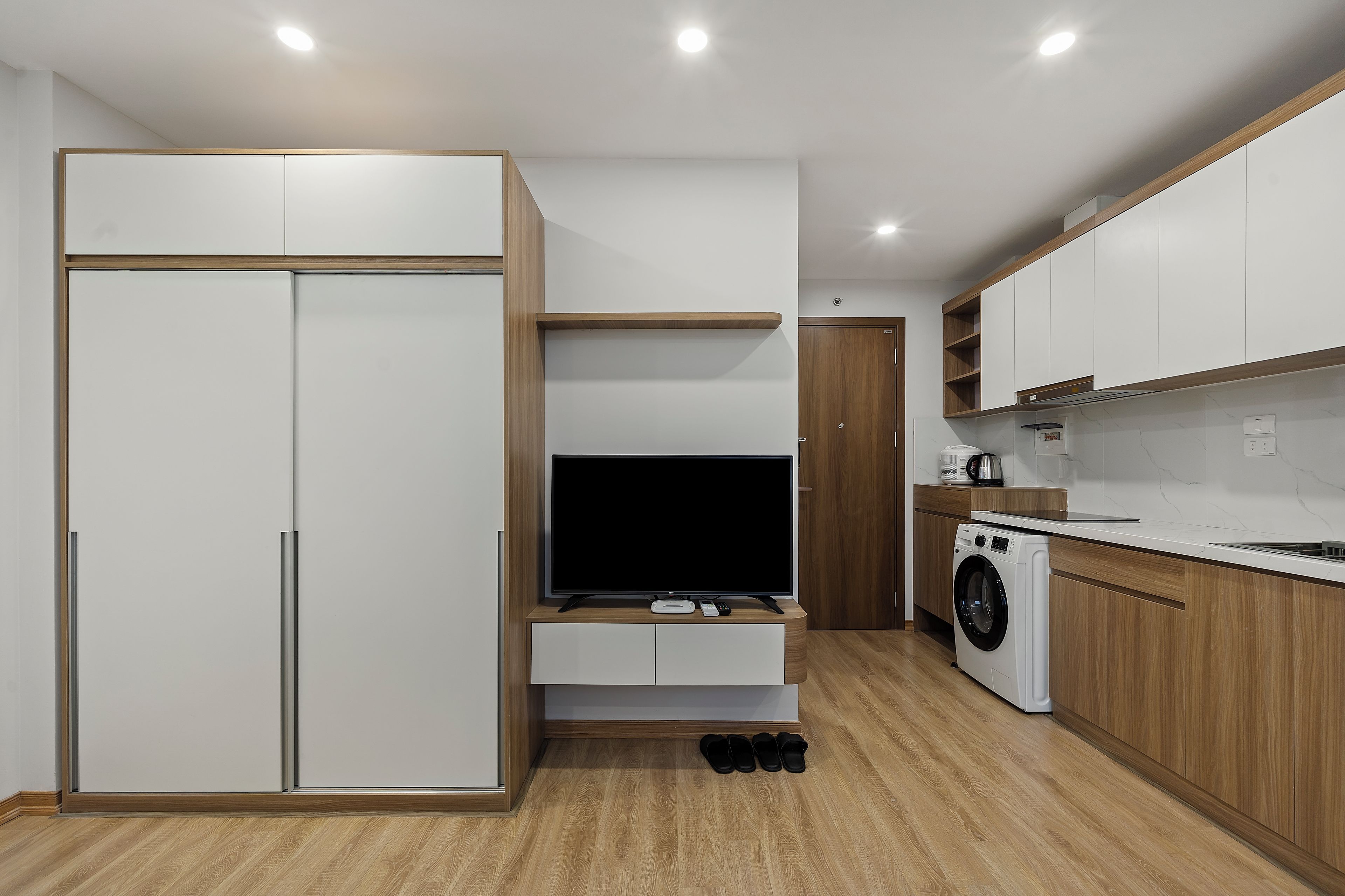 A modern kitchen with built-in appliances, a flat-screen TV, and wooden cabinetry.