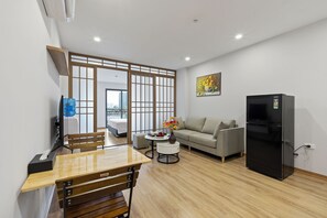 A modern living room with a wooden dining table, a sofa, a black refrigerator, and a TV. - 22housing Residence Suites (Hanoi)