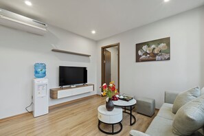 A modern living room with a flat-screen TV, a water dispenser, a round coffee table with a vase of flowers, and a grey sofa. - 22housing Residence Suites (Hanoi)