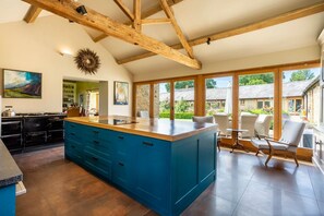 A spacious kitchen with a large island, wooden beams, and a view of the garden.