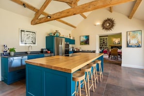A spacious kitchen with a large island, wooden beams on the ceiling, and a view into the dining area.