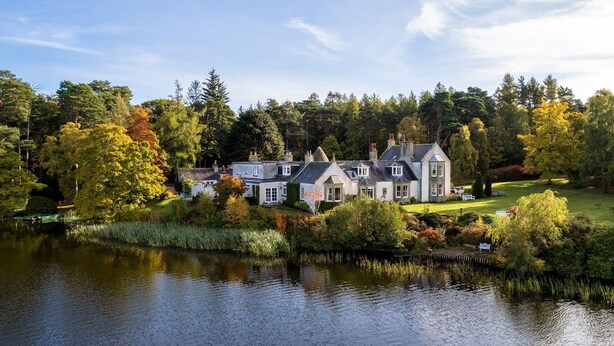 Ein großes, mehrstöckiges Haus mit Blick auf einen See, umgeben von Bäumen und Grünpflanzen.
