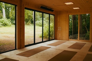 A room with large windows, wooden flooring, and yoga mats.