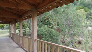 Une terrasse en bois dotée d’une balustrade, qui donne sur un jardin où l’on peut admirer différentes plantes et arbres.