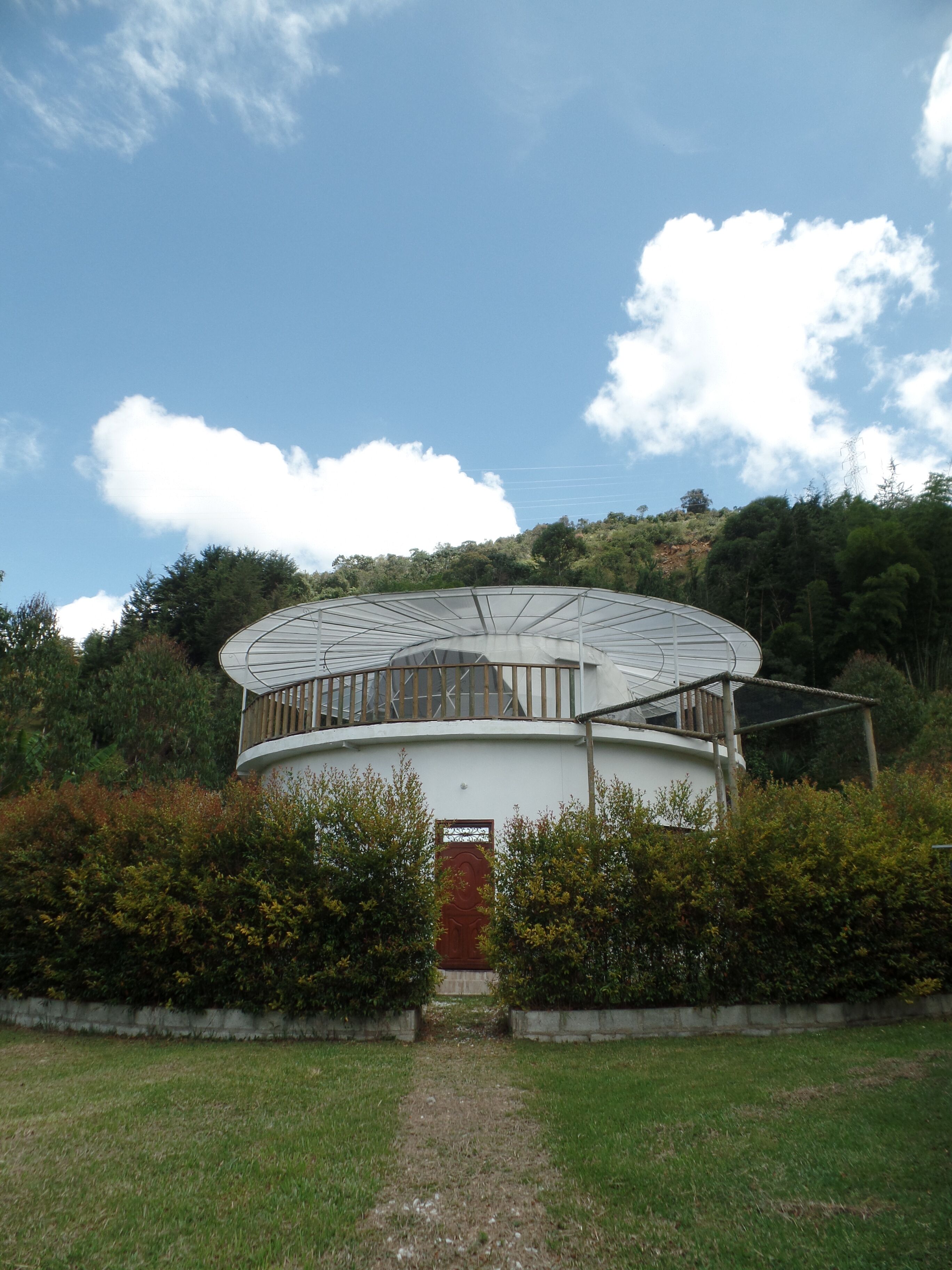 A circular building with a central door, surrounded by a garden and a pathway leading to it.
