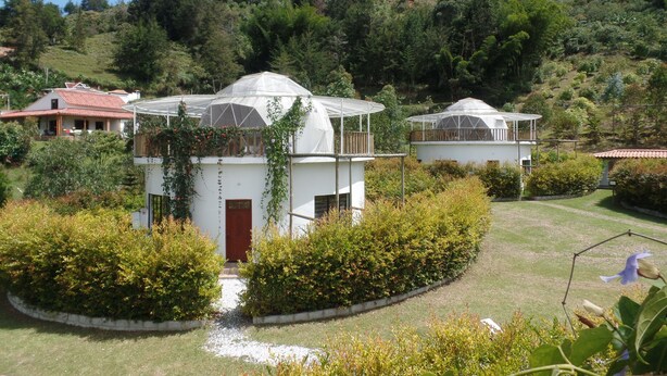 Un bâtiment blanc surmonté d’un dôme, entouré d’une végétation luxuriante et avec une colline en arrière-plan.