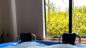Un bain à remous avec des jets de bulles, deux fauteuils et une fenêtre donnant sur un paysage verdoyant.