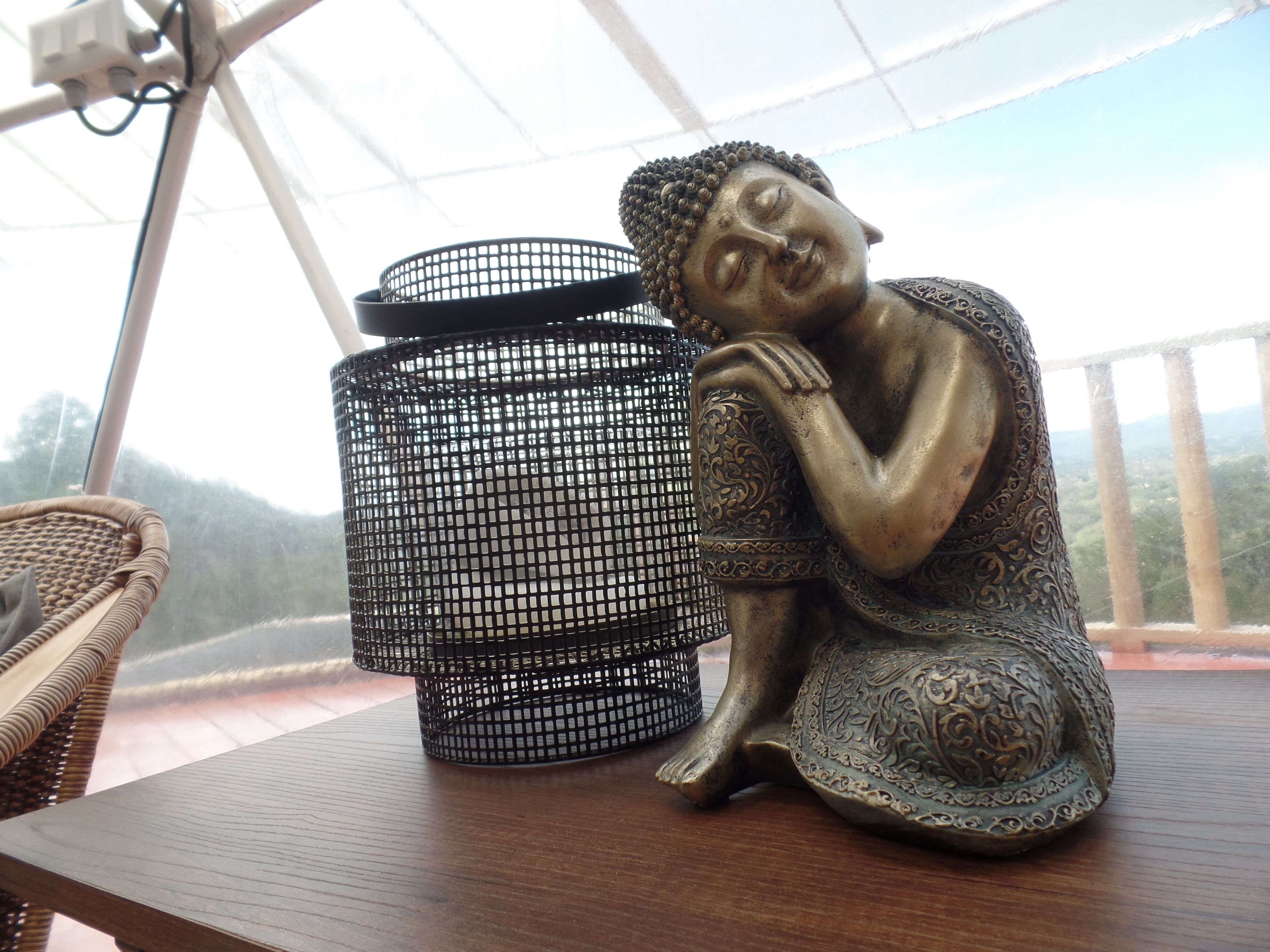 A Buddha statue on a wooden table with a decorative metal container beside it.