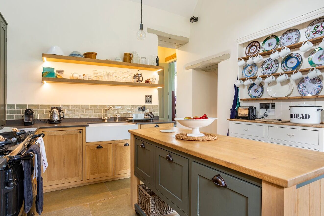 A kitchen with wooden cabinets, a sink, a countertop with a bowl of fruit, and a wall-mounted display of plates and cups.