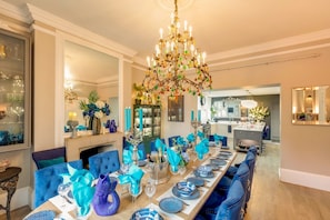 A dining room with a long table set for six, blue upholstered chairs, a chandelier, and a mirror on the wall.