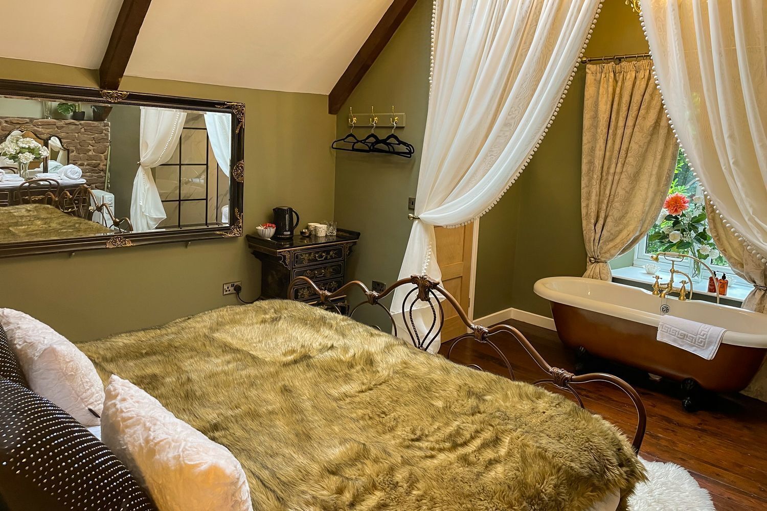 Ein Schlafzimmer mit einem großen Bett, einer Badewanne im Vintage-Stil und einem Fenster mit Vorhängen.