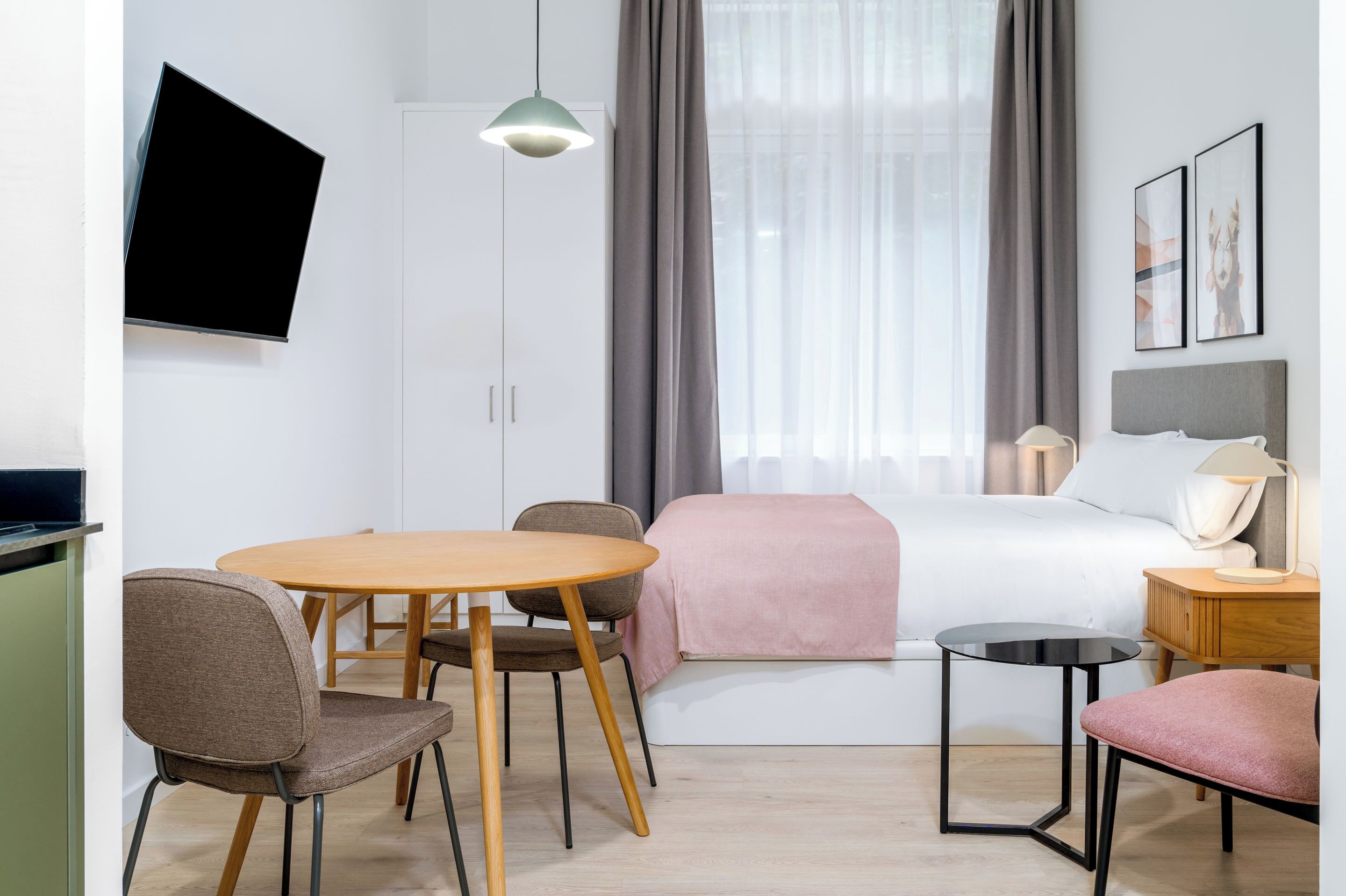 Habitación de hotel moderna con cama, escritorio, silla, televisor y ventana con cortinas.