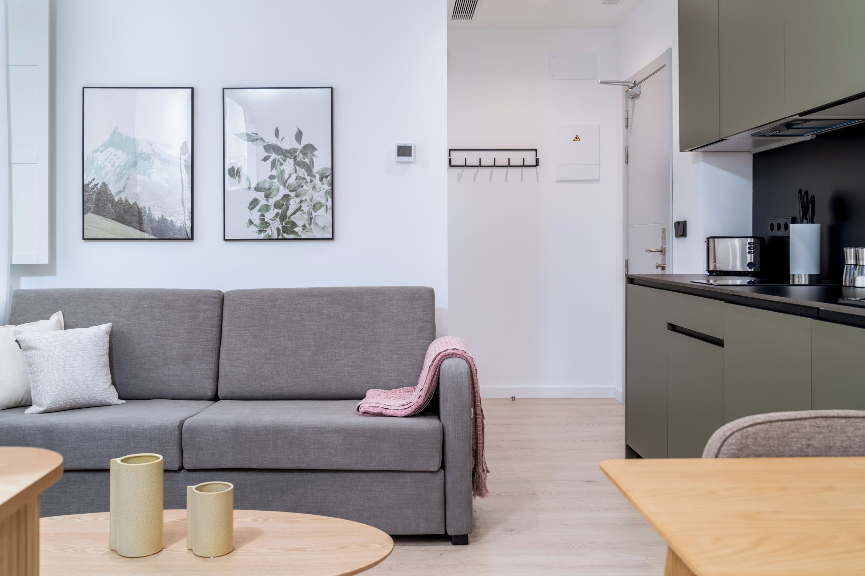 Ein modernes Wohnzimmer mit einem grauen Sofa, einem Holztisch und einer Küchenzeile mit Herd und Schränken.