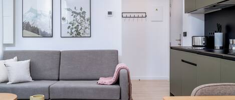 Una sala de estar moderna con un sofá gris, una mesa de centro de madera y una cocina con estufa y armarios.