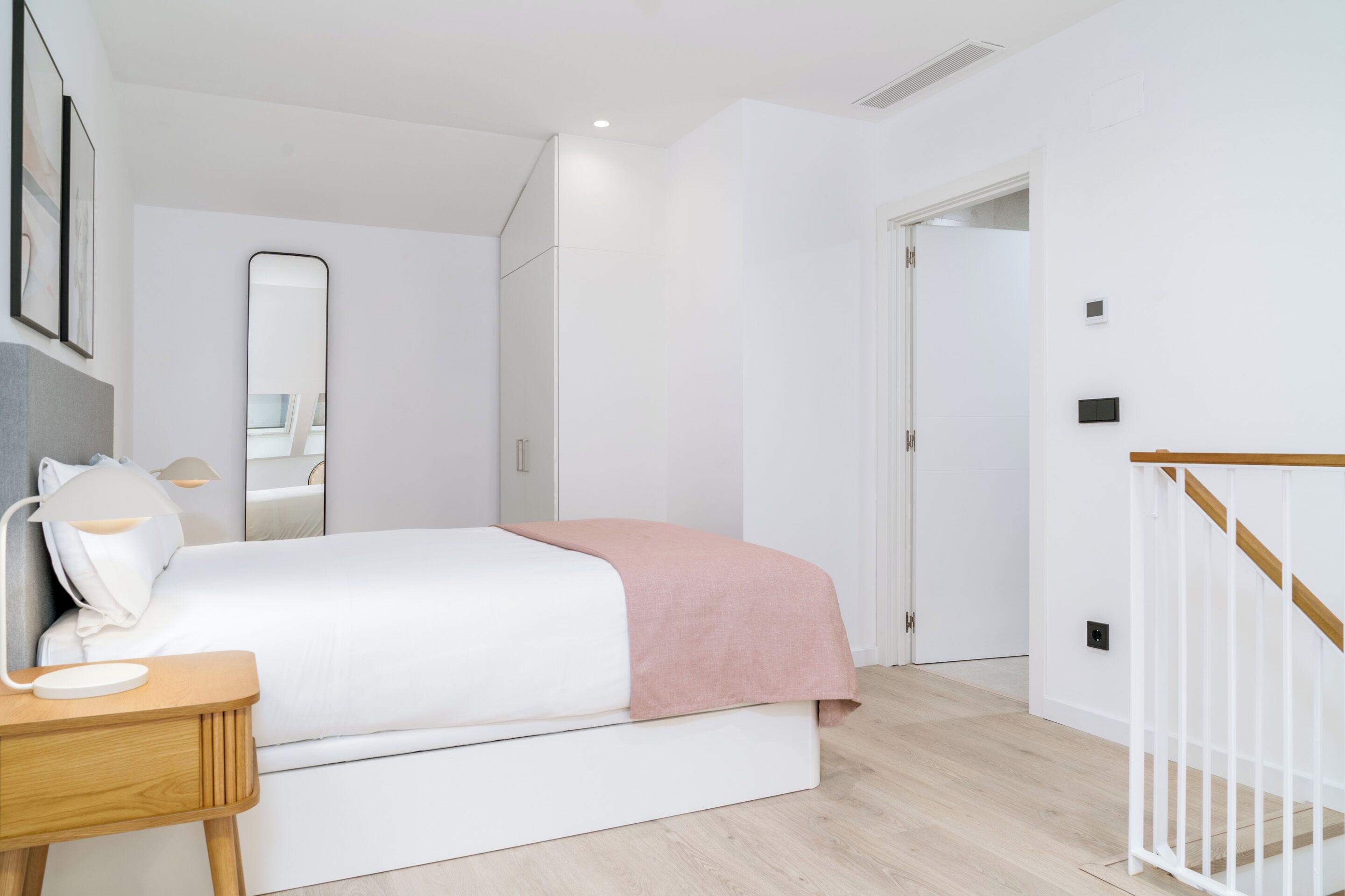 Une chambre à coucher moderne avec un lit, une table de chevet, une lampe et un miroir.