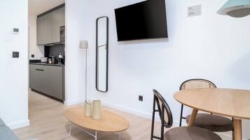 Una cocina moderna con armarios grises, un televisor de pantalla plana montado en la pared y un comedor con mesa y sillas de madera.