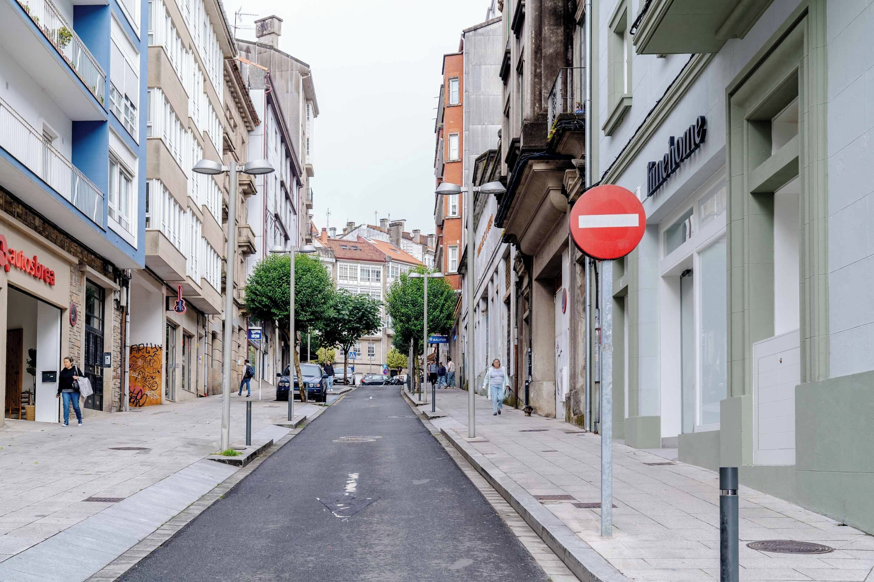 Una estrecha calle urbana flanqueada por edificios de varios pisos, una señal de prohibido el paso y peatones.