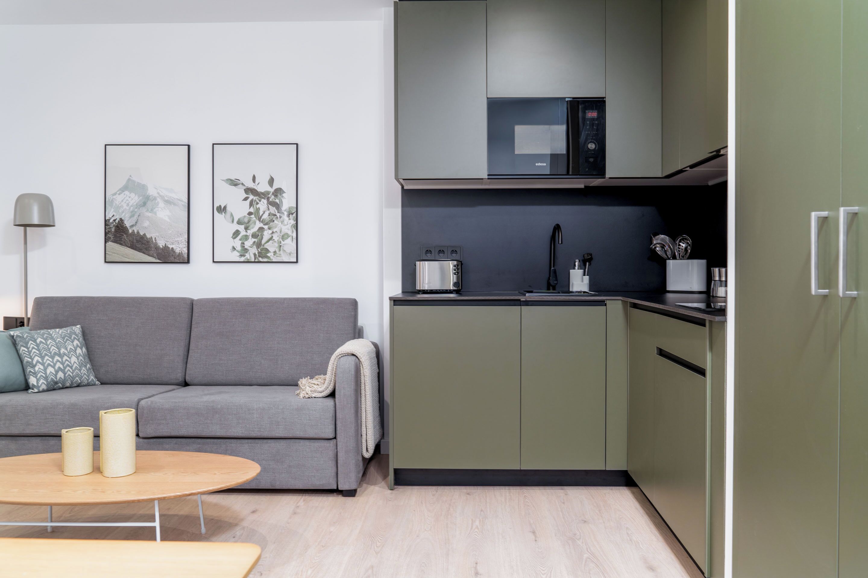 Una cocina moderna con armarios verdes, un sofá gris y una mesa redonda de madera.