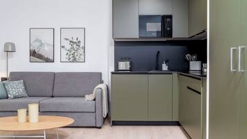 Una cocina moderna con armarios verdes, un sofá gris y una mesa redonda de madera.