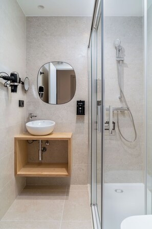 A modern bathroom with a glass-enclosed shower, a wooden vanity with a white sink, and a round mirror. - Limehome Santiago de Compostela (Santiago de Compostela)