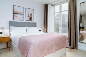 A modern hotel room with a large bed, two bedside tables, a window with curtains, and artwork on the wall. - Limehome Santiago de Compostela (Santiago de Compostela)