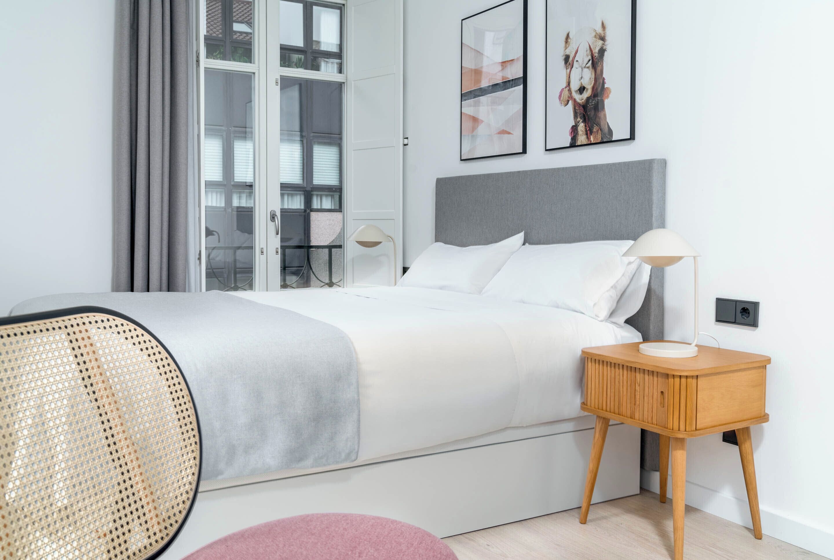 A modern bedroom with a bed, bedside table, lamp, and a view of the outside.