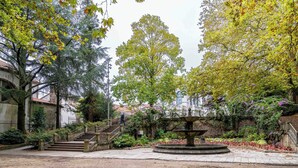 Pátio com uma fonte central, cercado por árvores e uma escadaria que leva a um andar superior.