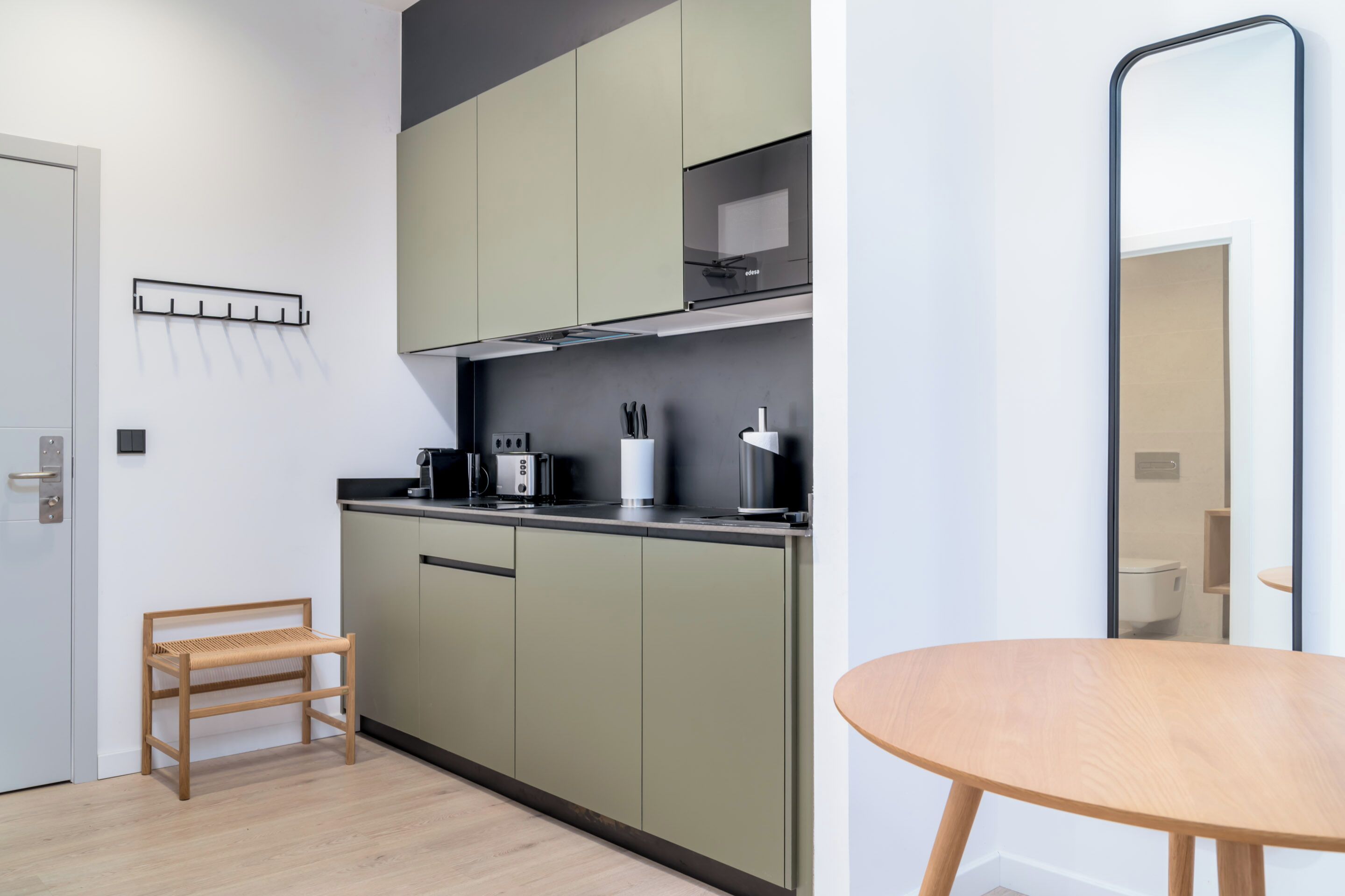 A modern kitchen with green cabinets, a wooden bench, and a round table.
