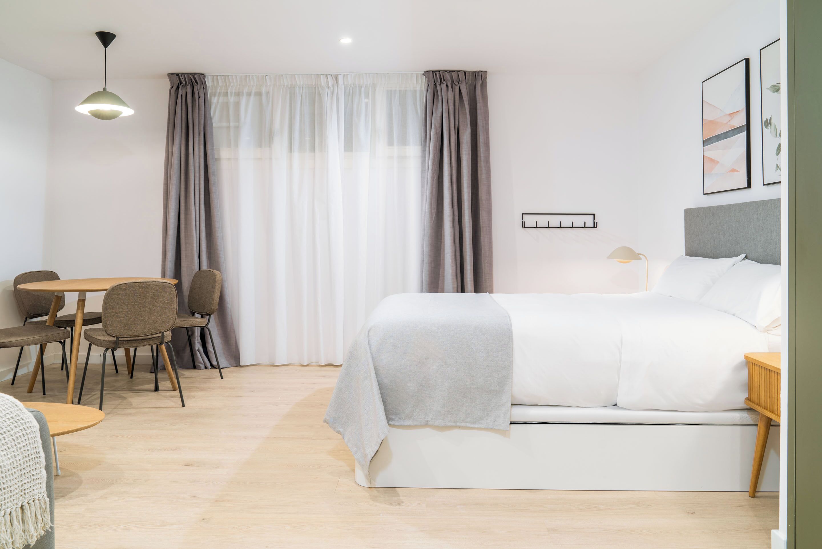 Una habitación de hotel moderna con una cama, una mesa de comedor con sillas y un ventanal con cortinas.