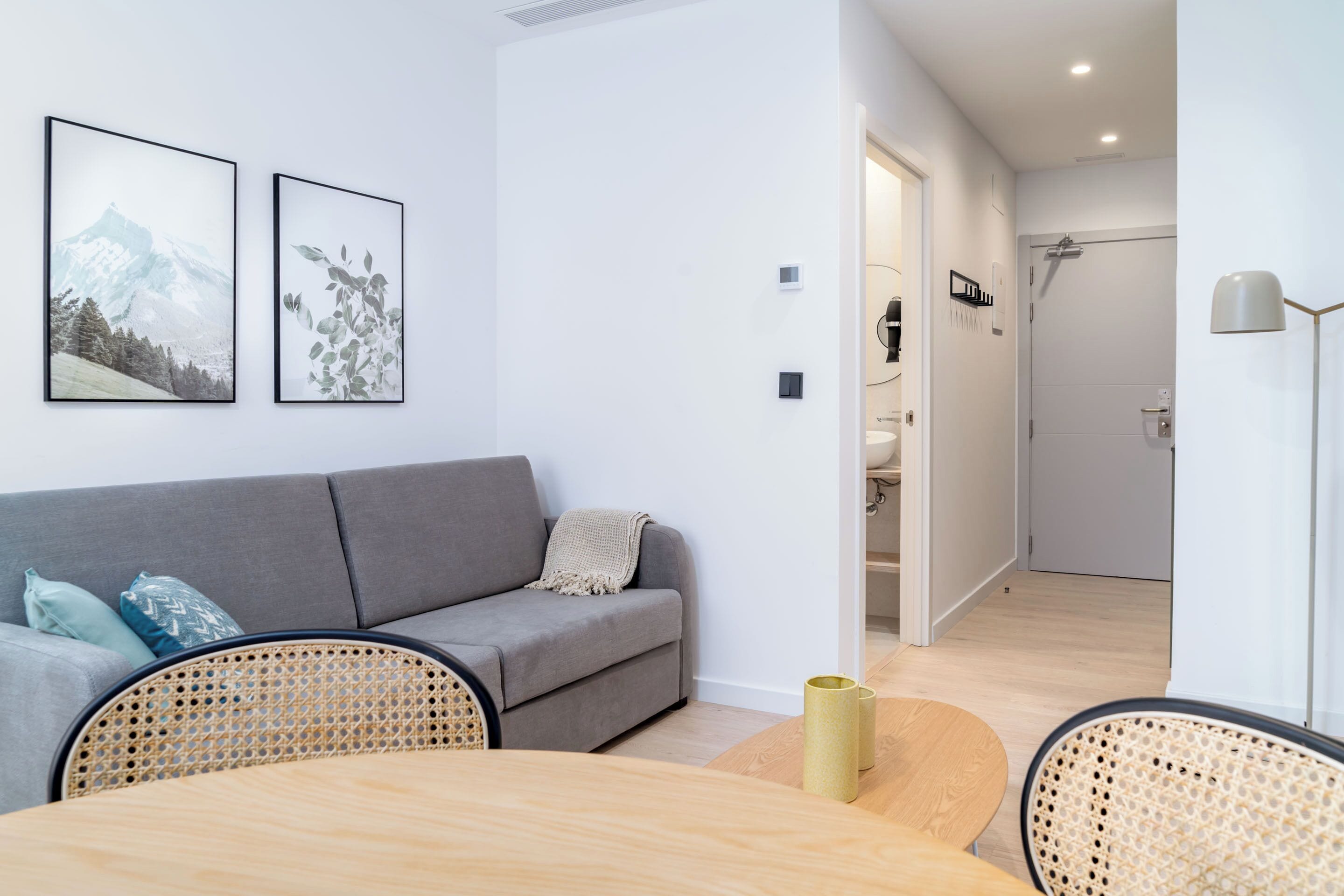 A modern living room with a grey sofa, two framed pictures, a dining table with chairs, and a wooden floor.