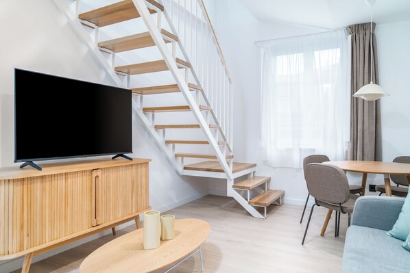 A modern living room with a flat-screen TV, wooden furniture, a staircase, and a dining area. - Limehome Santiago de Compostela (Santiago de Compostela)