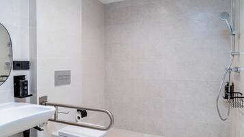Un baño moderno con lavamanos, inodoro y zona de ducha blancos.