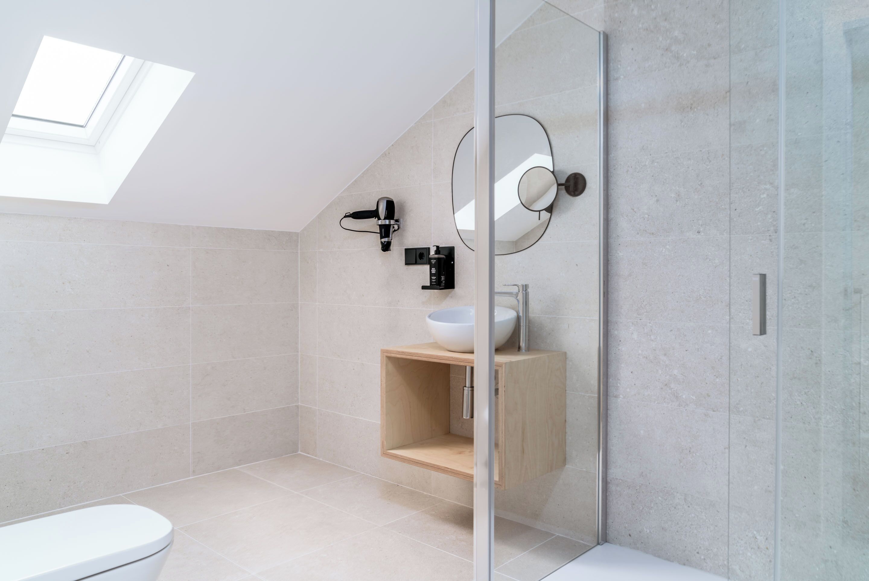 Une salle de bain moderne avec un puits de lumière, un lavabo blanc et un meuble-lavabo en bois.