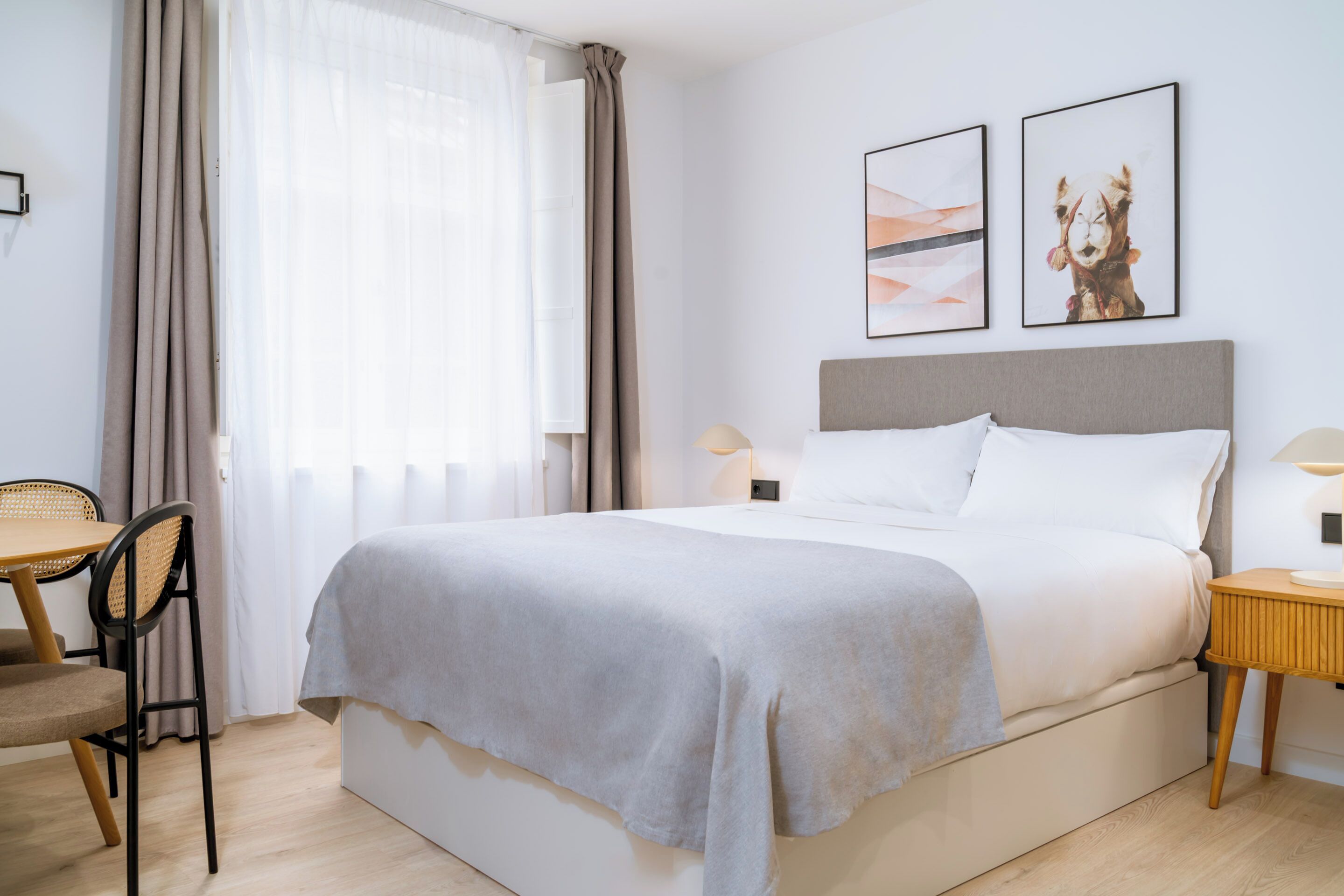 Una habitación de hotel con una cama, una silla, una mesita de noche y dos cuadros en la pared.