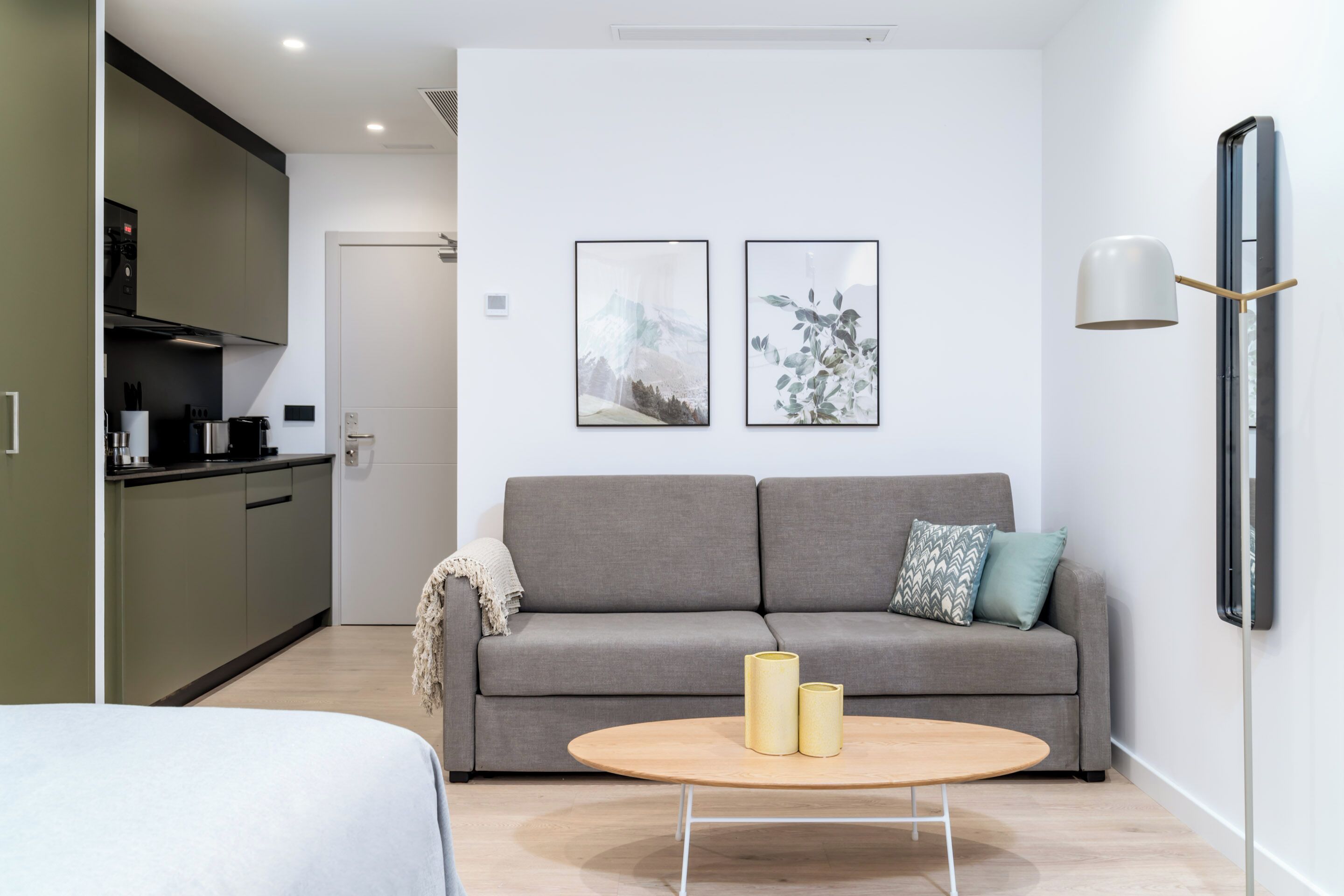 A modern living room with a grey sofa, two framed pictures on the wall, a round coffee table with two candles, and a minimalist lamp.